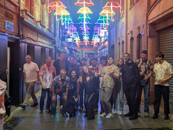 Group of friends posing under colorful umbrella lights in alley.