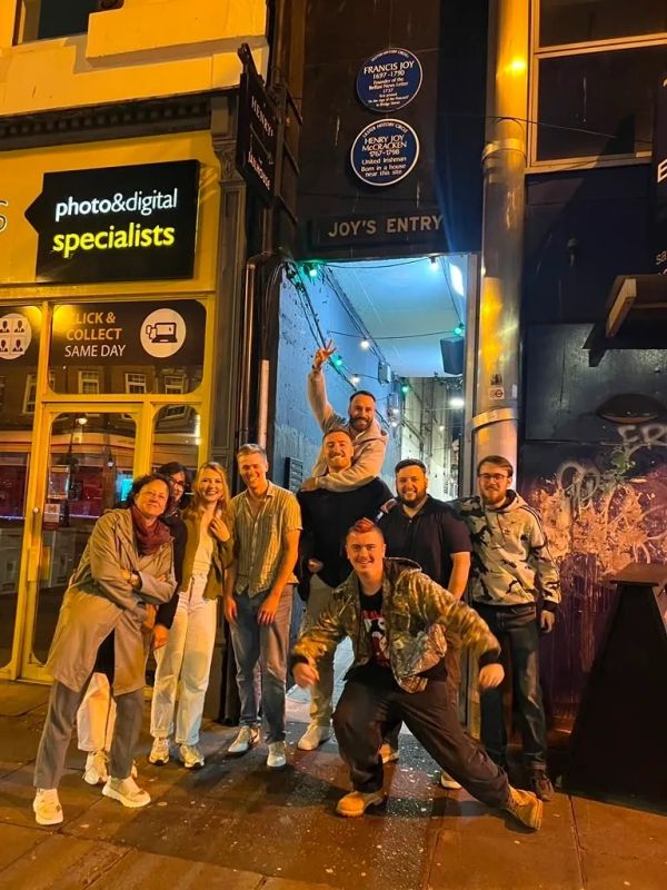 Group of friends posing happily outside a photo and digital shop at night.