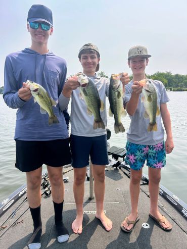 Three boys holding fish on a boat by the water.