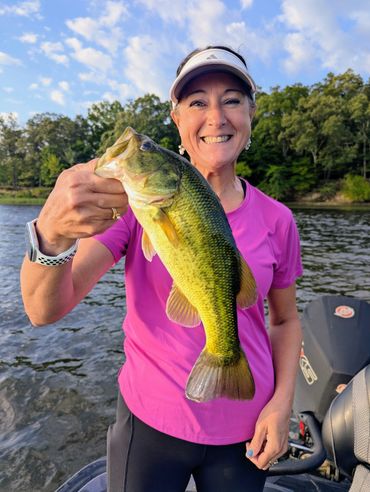 Woman holding a largemouth bass fish with a smile on a boat.