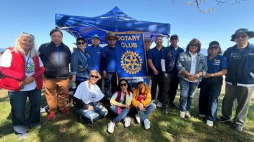 Group of people gathered outdoors under a Rotary Club tent on a sunny day.