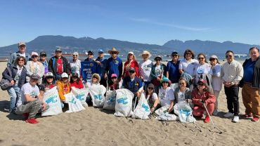 Group of people posing on a beach with trash bags for a cleanup event.