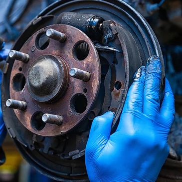 A mechanic wearing blue gloves inspecting a car brake drum.