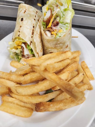 Chicken wrap with lettuce, cheese, and fries on a white plate.