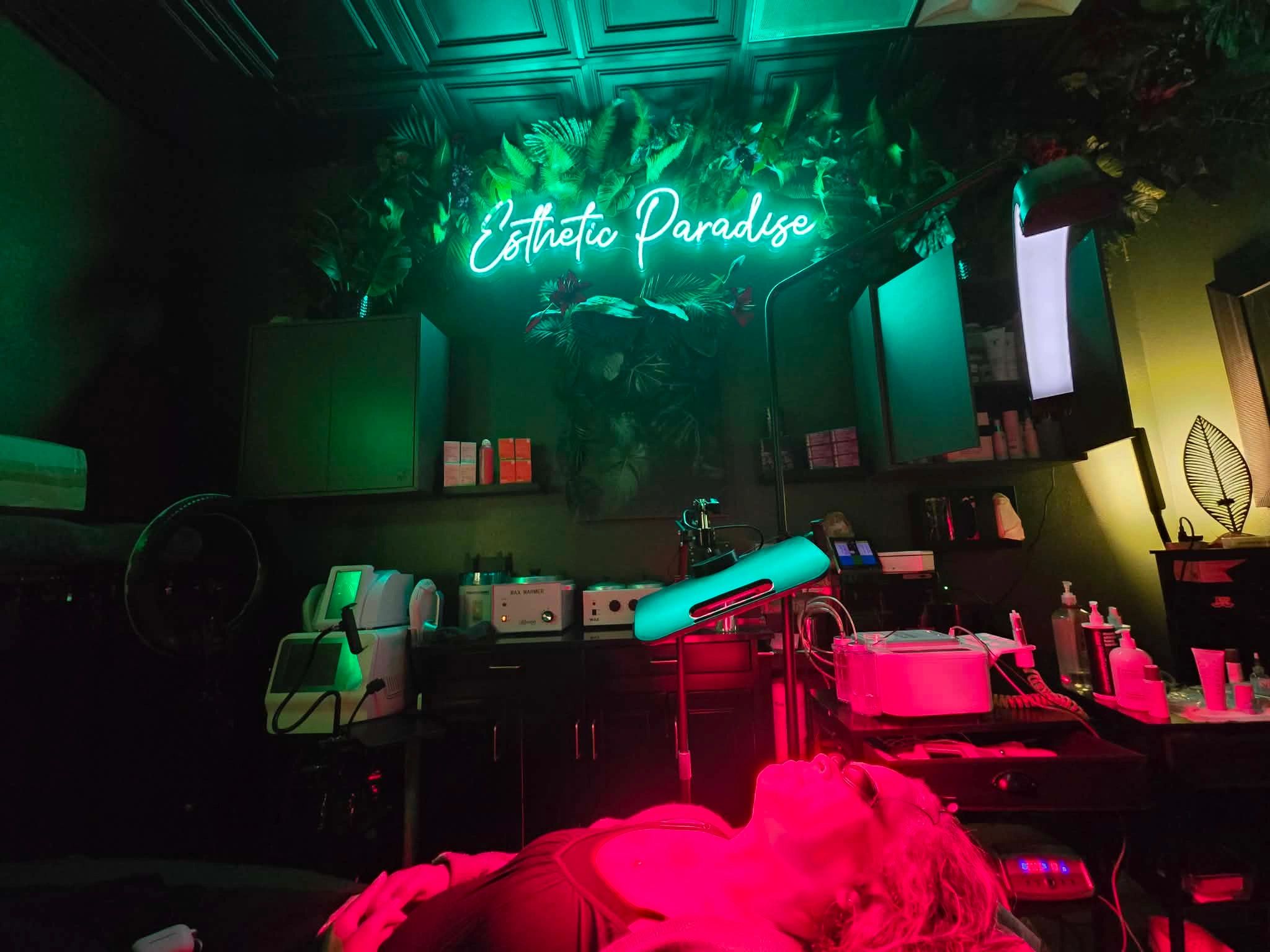 Neon sign "Esthetic Paradise" in a spa room with glowing lights and a reclining person.
