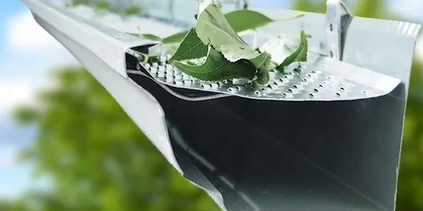 Leaves caught in a damaged metal gutter outdoors.