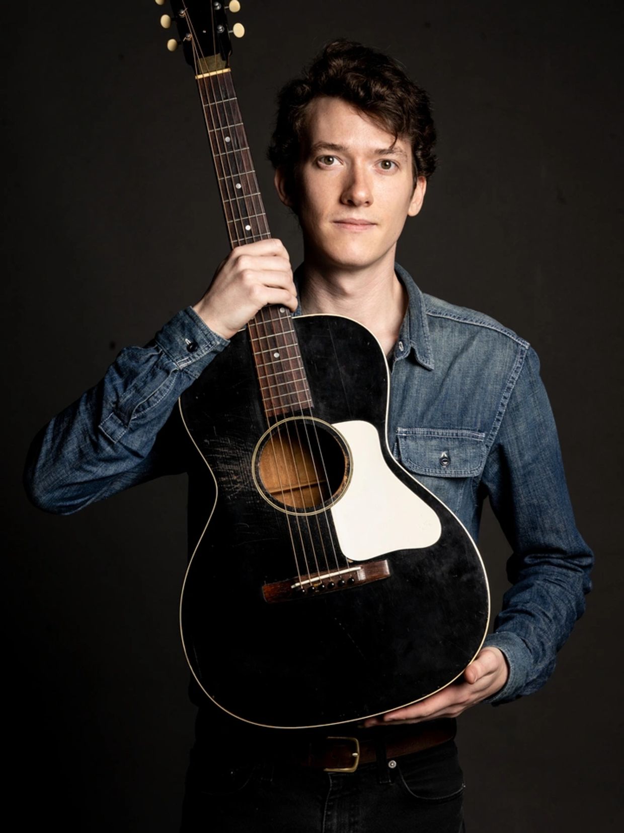 Headshot of Bluegrass and Folk music artist Mason Via, holding his vintage tuxedo Gibson guitar.