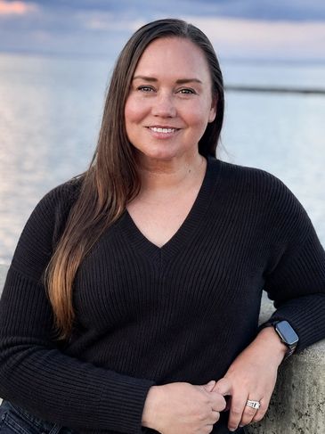 Smiling woman in black sweater by the water at sunset.
