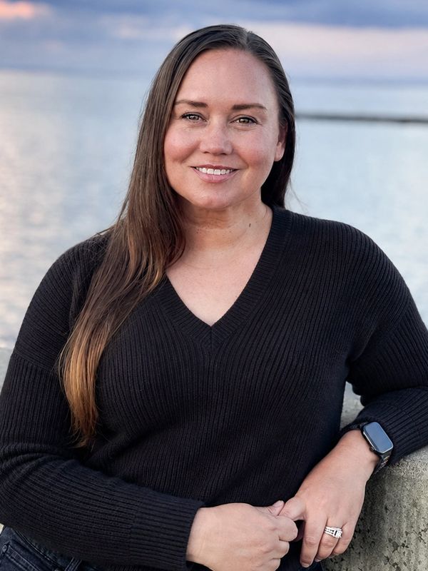Smiling woman in black sweater by the water at sunset.