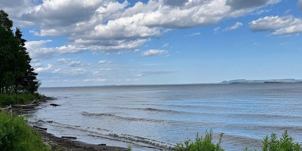 Calm shoreline with gentle waves and a cloudy blue sky.