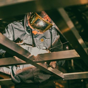 Welder working on metal framework with protective gear.