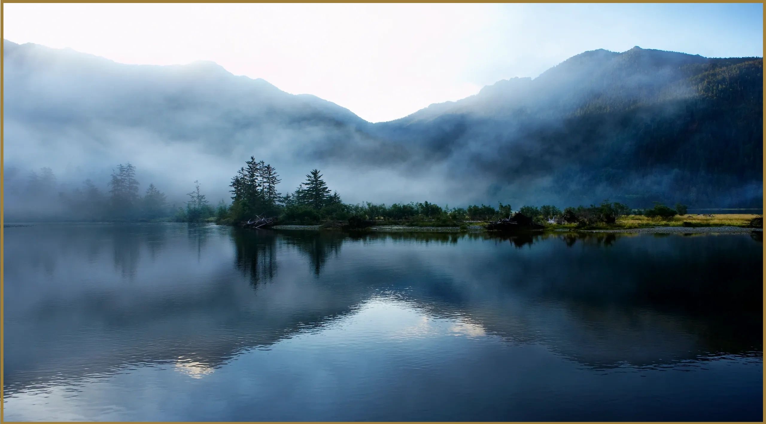 Misty mountains reflecting on calm water.