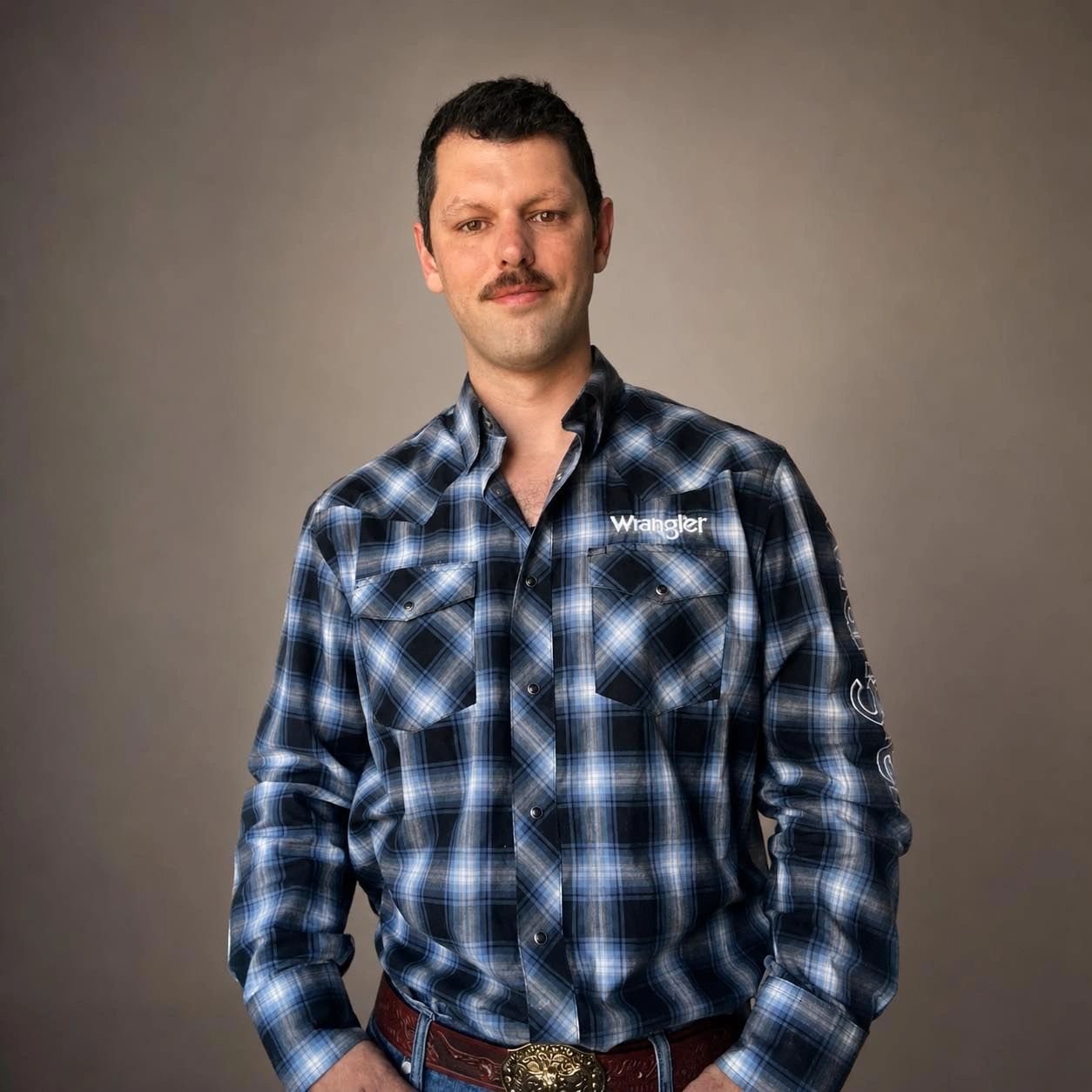 Man in a blue plaid Wrangler shirt with a mustache and cowboy belt.