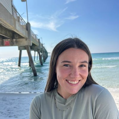 Smiling woman posing near a pier by the ocean on a sunny day.
