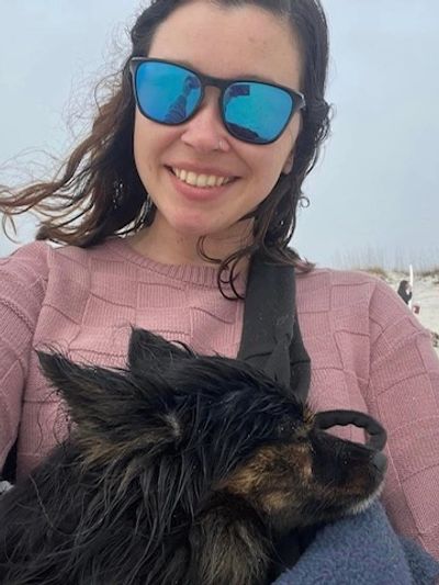 Woman in sunglasses smiling with a small dog wrapped in a blanket.