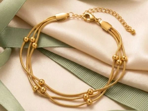 Delicate gold bracelet with spherical beads on a silky fabric.