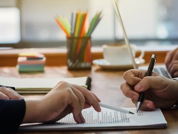 Two people reviewing and signing a document together at a desk.