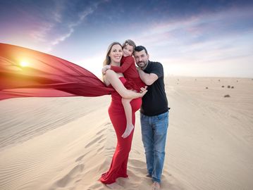 Dad hugs pregnant mom who holds daughter while mom's dress flies over the dunes at sunset