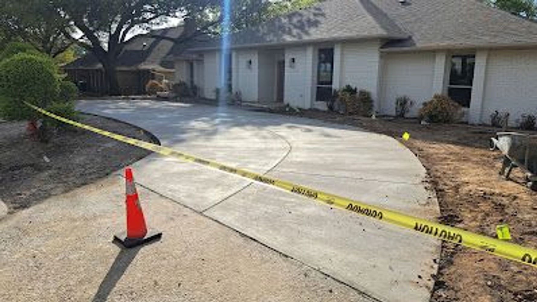Newly poured concrete driveway cordoned off with caution tape and an orange traffic cone.