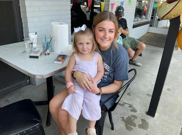 A young woman hugs a little girl sitting on her lap at an outdoor table.