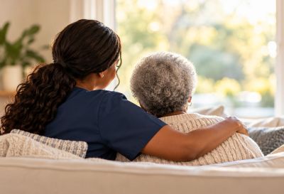 Caregiver comforting an elderly woman on a couch.