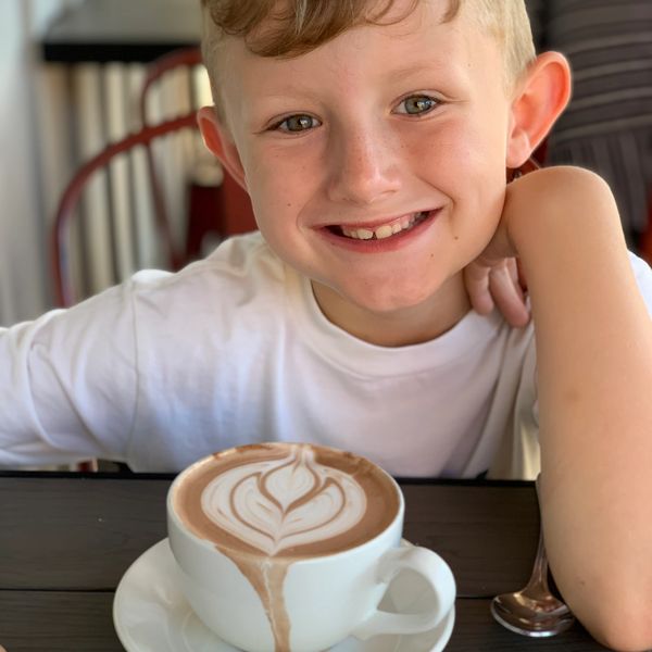 Smiling boy with a cup of latte featuring heart-shaped foam art.