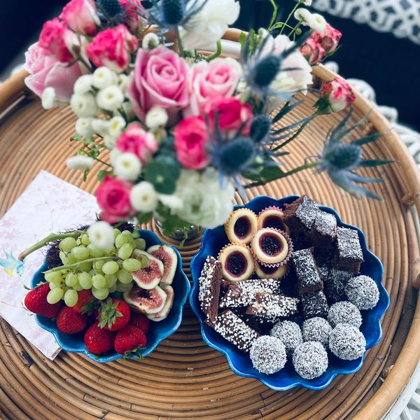 Colorful flower bouquet with plates of fresh fruits and assorted sweets on a wicker table.