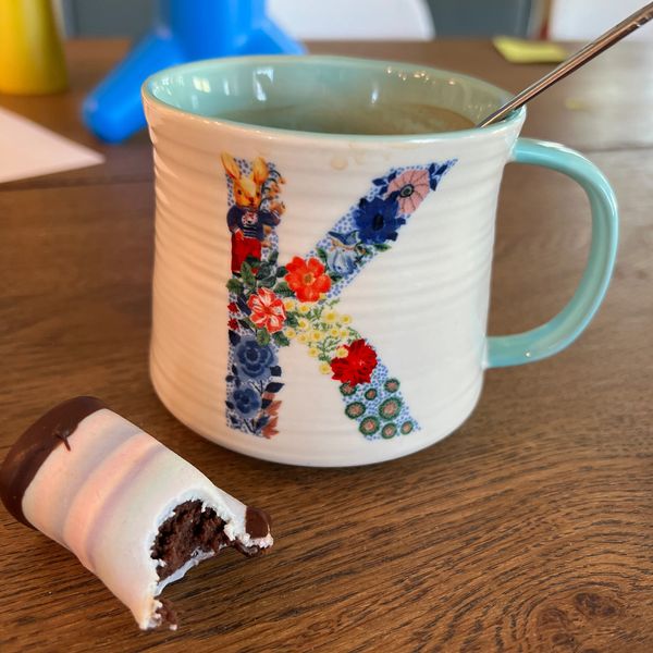 Floral-patterned mug with letter 'K' and a partially eaten chocolate treat.