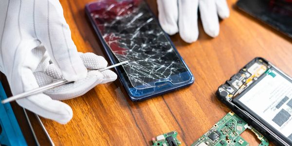 Technician repairing a smartphone with a cracked screen and exposed circuit boards.