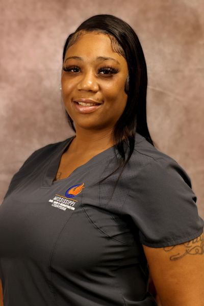 Smiling woman in gray medical scrubs with Mississippi College logo.