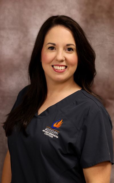 Smiling woman in dark blue scrubs with Mississippi College logo.