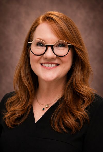 Smiling woman with red hair and round glasses against a brown background.