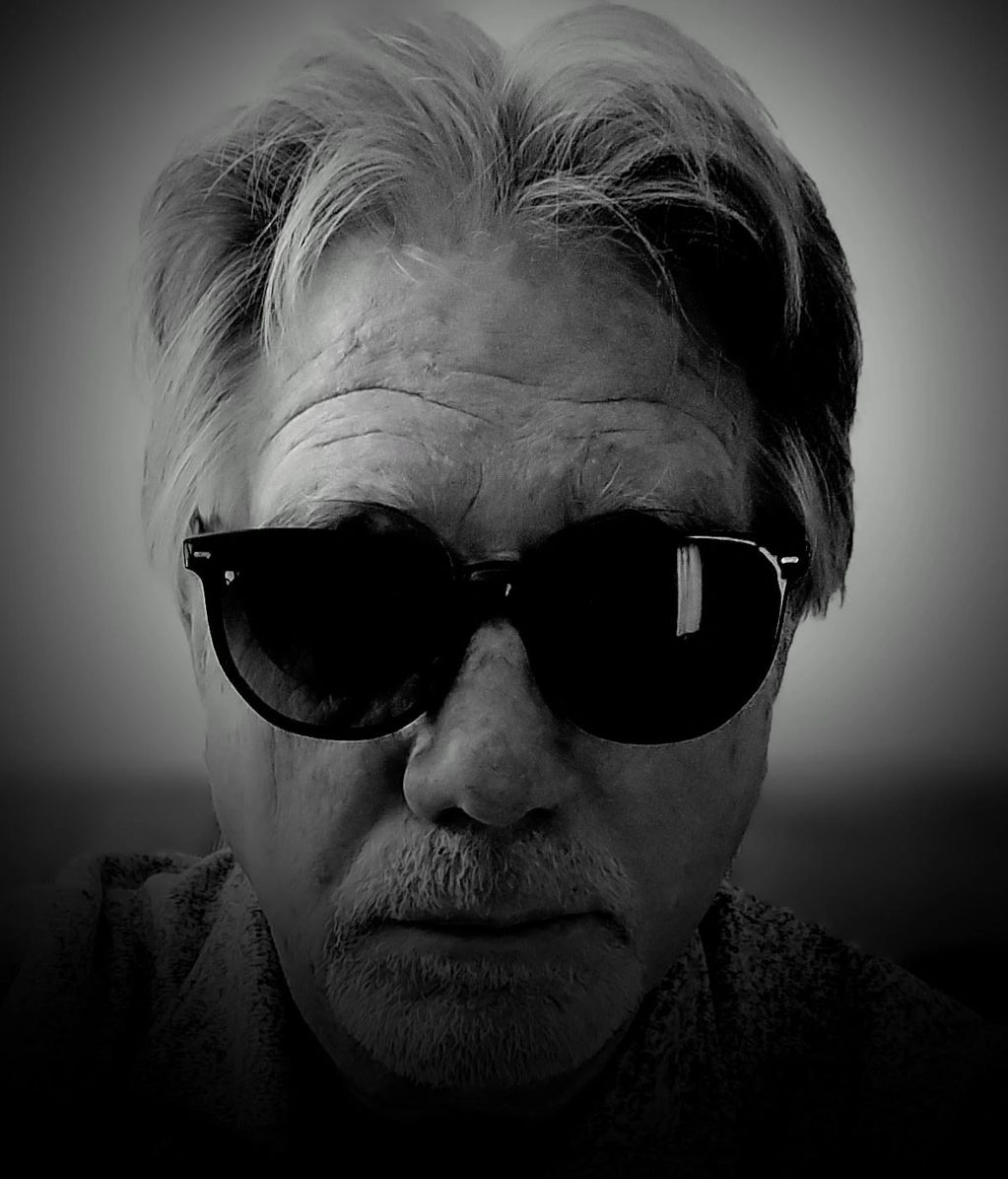 Black and white portrait of a man wearing dark sunglasses.