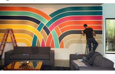 Man painting a colorful retro-style geometric mural in a modern living room.