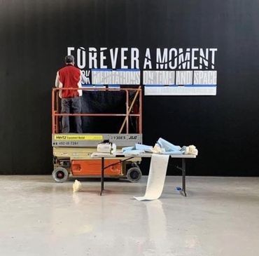 A worker installs large text on a black wall using a lift and table.