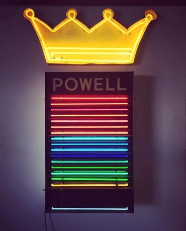 Neon sign with a yellow crown above rainbow-colored horizontal lines and the word POWELL.