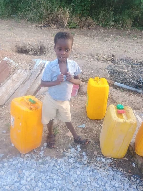 Young boy standing near yellow water containers.