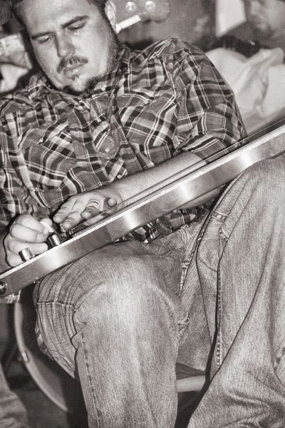 Man tuning guitar focused on adjustment.