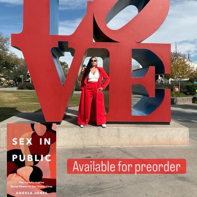 Angela Jones is wearing a red suit with a floor-length jacket and a white crop top. 