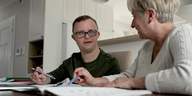 A young man with Down syndrome studying with an older woman at a table.