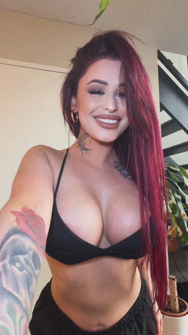 Smiling woman with long red hair and tattoos wearing a black bikini top.