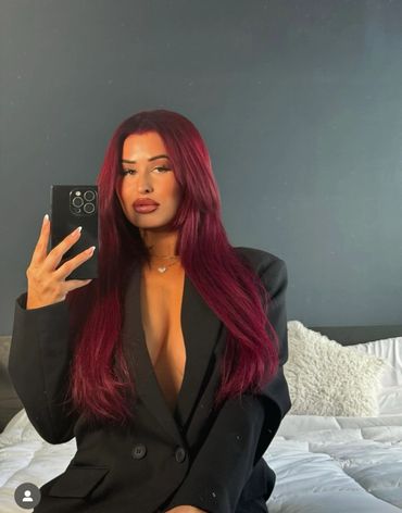Woman with long red hair taking a mirror selfie in a black blazer.