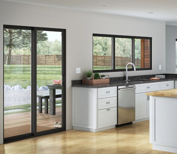 Modern kitchen with white cabinetry, black countertops, and large windows overlooking a backyard.