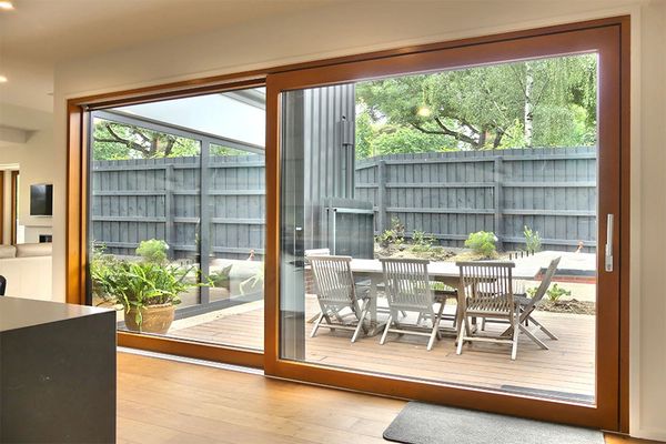 Modern sliding glass door opens to a wooden patio with outdoor seating and greenery.