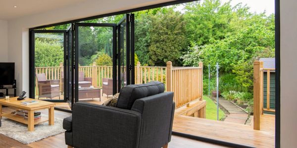 Modern living room with large folding glass doors opening to a wooden deck and lush garden.