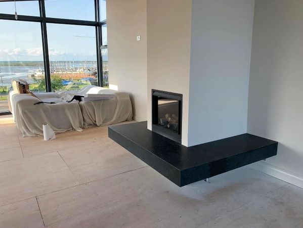 Modern room with a suspended black fireplace and covered furniture near large windows.
