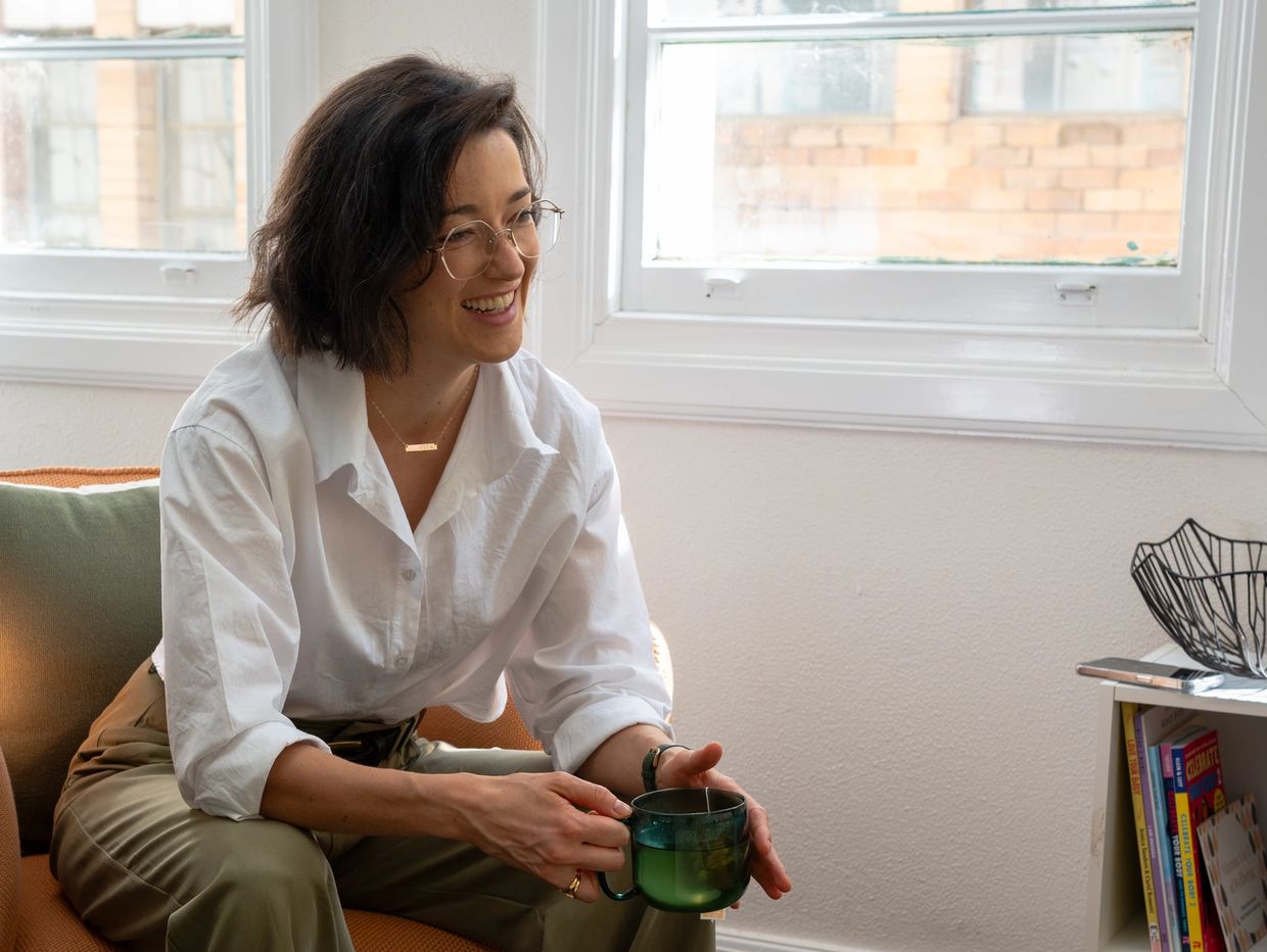 Courtney is sitting on a chair leaning forward with a cup of tea.