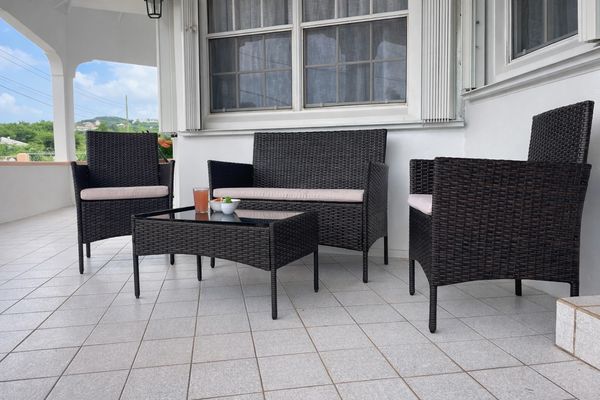Outdoor wicker patio furniture set with two chairs, a loveseat, and a table on a tiled porch.