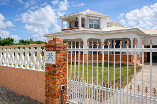Large white house with a gated brick and white fence under a blue sky.
