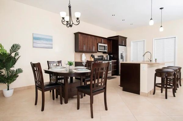 Modern kitchen and dining area with dark wood furniture and beige tiles.